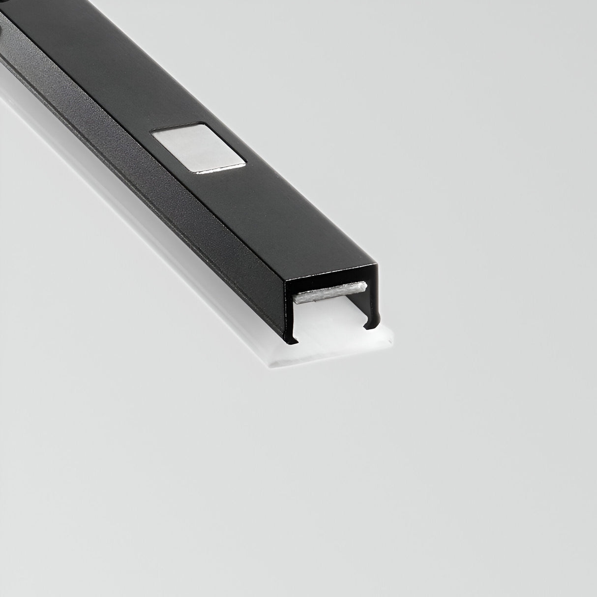 Close-up of the Linear LED Surface-Mounted Track Light 12W 3000K in black and white, showcasing its dimmable lighting feature with a small reflective rectangular area and a white insert extending from its open end, set against a plain gray background.