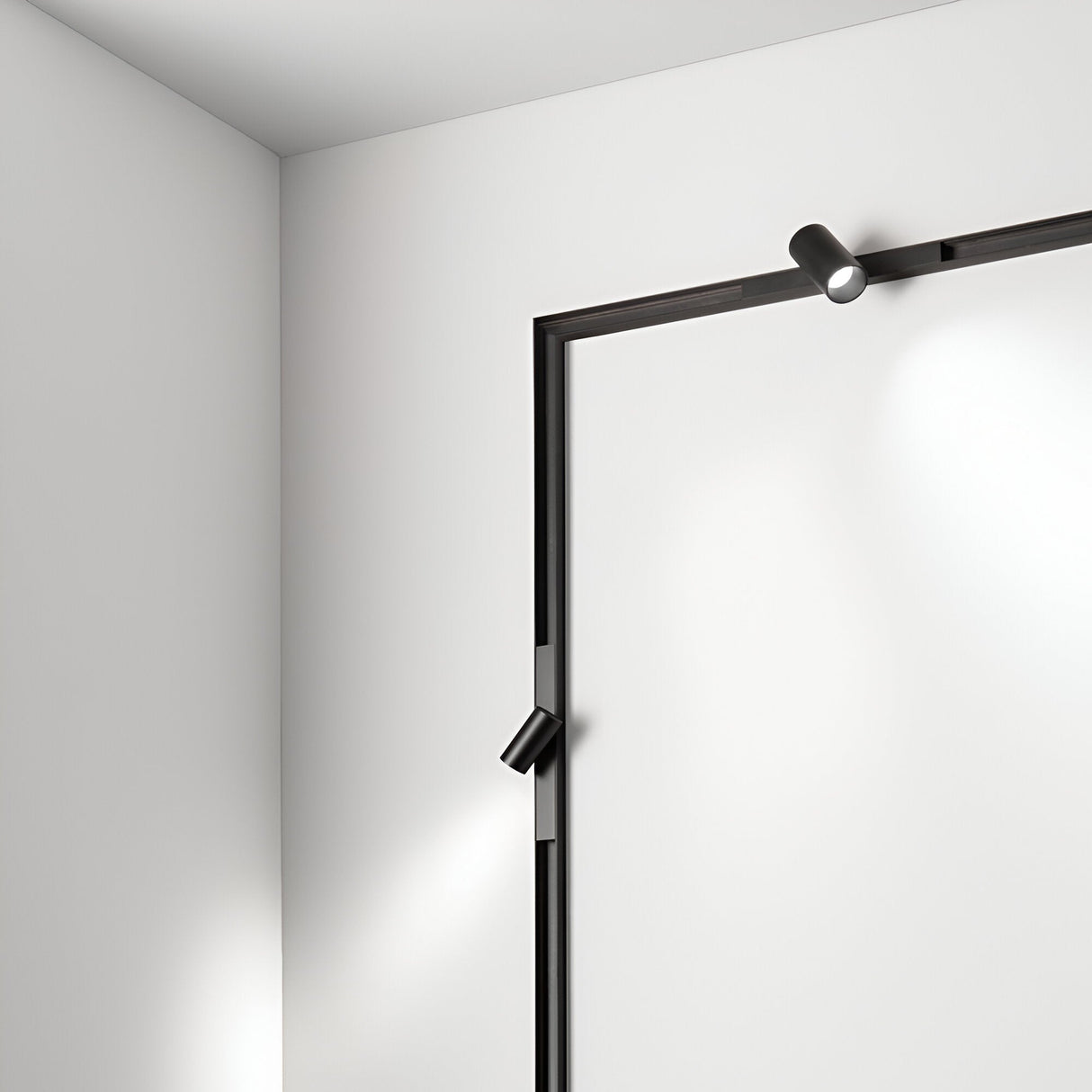 A minimalistic room corner showcases a white wall accented by two Viora Magnetic Dimmable LED Single Track Lights, featuring a sleek cylindrical design in black mounted on a recessed magnetic track. The 5W, 3000K lights create subtle shadows that beautifully highlight the modern, clean lines of the space.