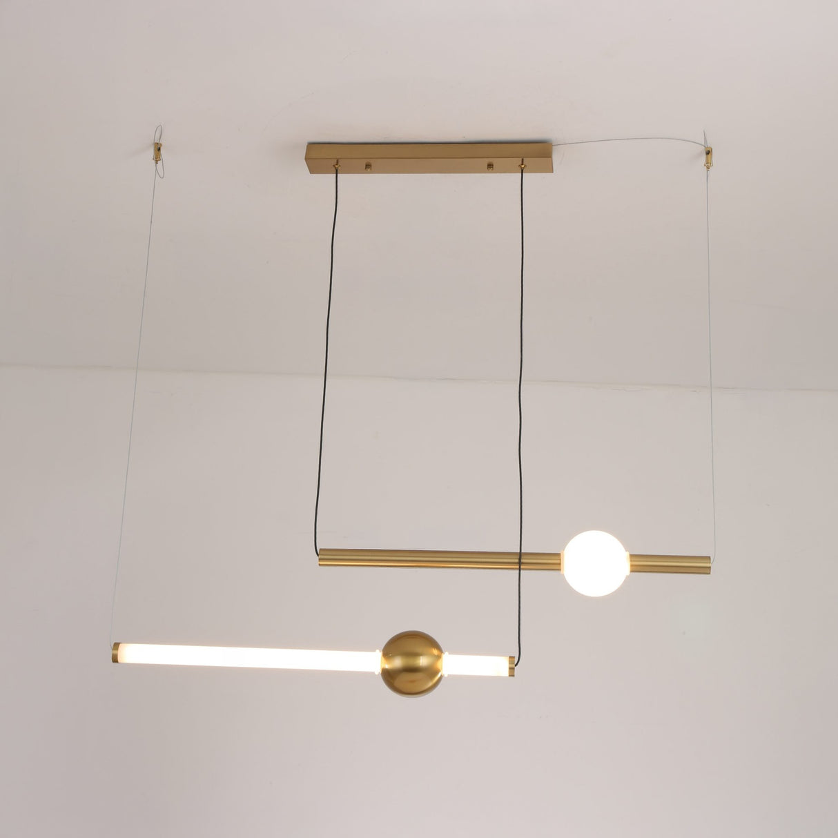 Niori Sottile LED horizontal suspension light with two slim brushed gold linear tubes and a frosted white opal globe, shown against a plain ceiling.
