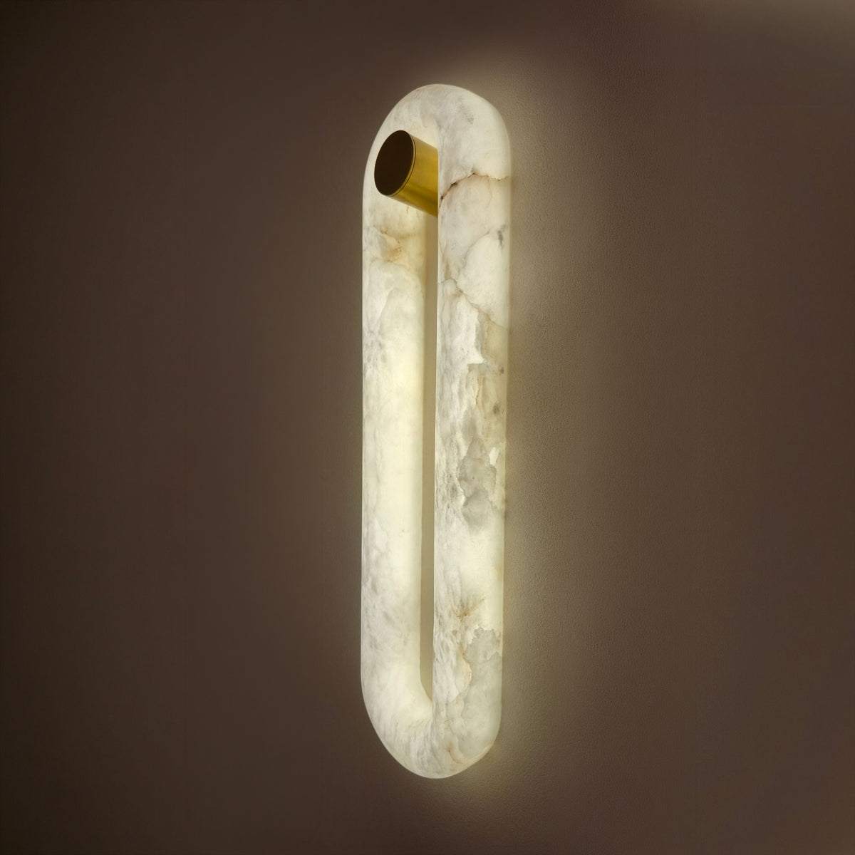 Serava LED Alabaster Wall Light Large in soft white, an elongated oval ring of natural alabaster with a brass cylindrical bracket, glowing warmly against a dark background.