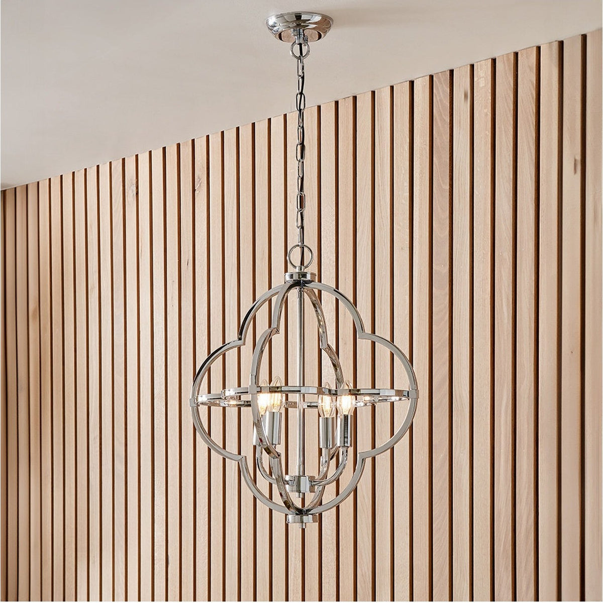 Amine Chrome 4 Light Fleur De Lys Pendant, 47cm, hanging from a chain with an open circular frame and four candle-style bulbs, shown against wood slat panelling.