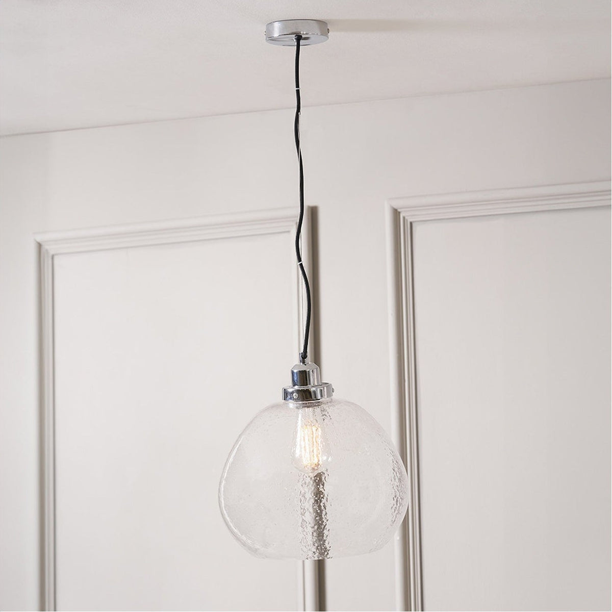 Beja Organic Shape Clear Bubble Glass Pendant Light, 30cm, with chrome fitting and exposed bulb, hanging from a black cord against a panelled white door.