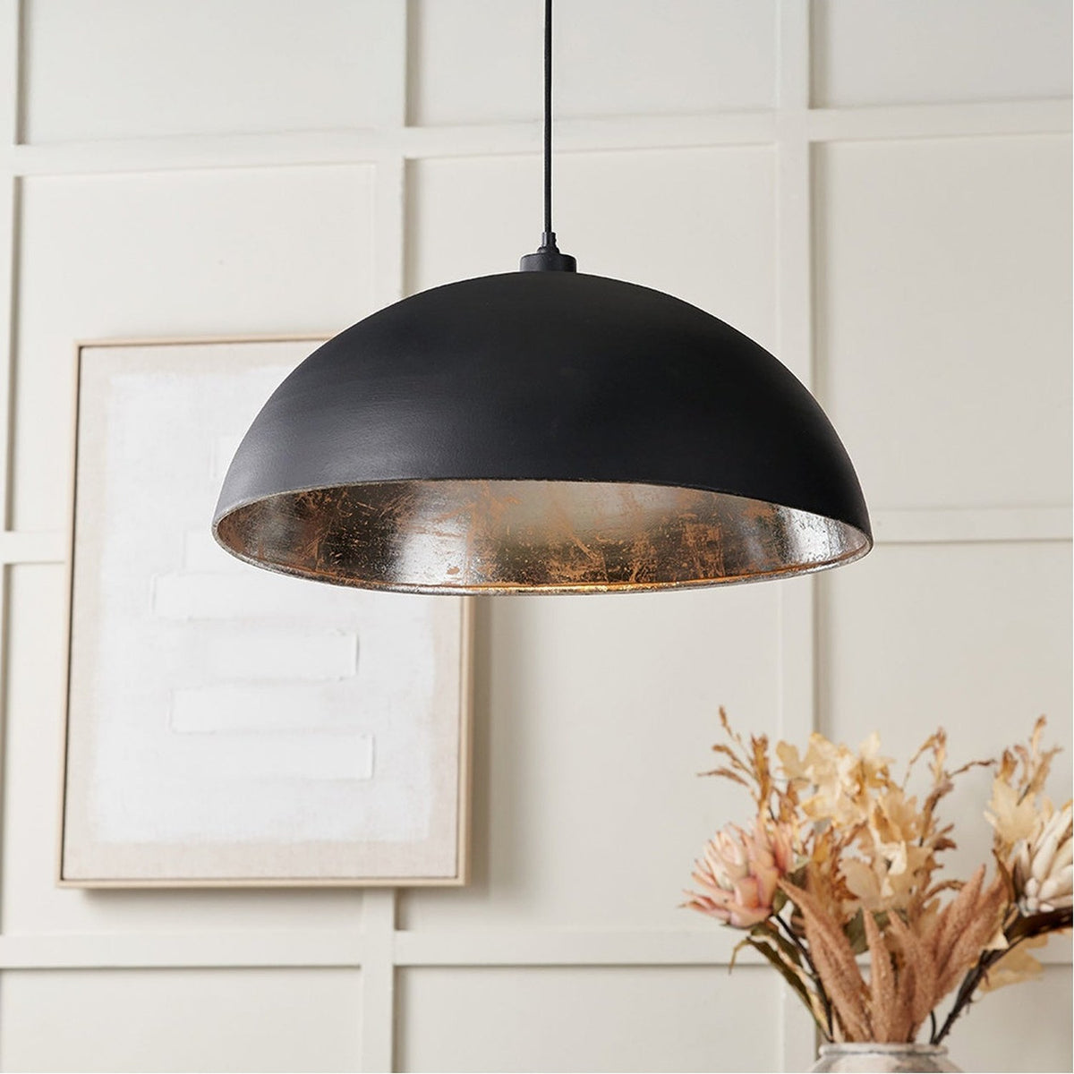 Anders 62cm dome pendant light in matt black iron with silver leaf interior, hung above a neutral dining area with framed art and dried flowers.