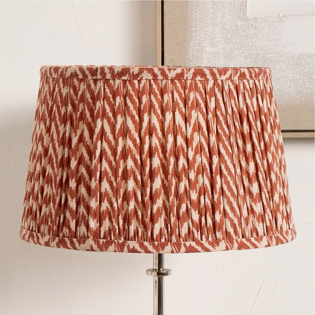 Vienna Red Chevron Pleated Lampshade, 30cm, in fabric with a red and cream zigzag pattern, shown fitted to a floor lamp against a light neutral background.