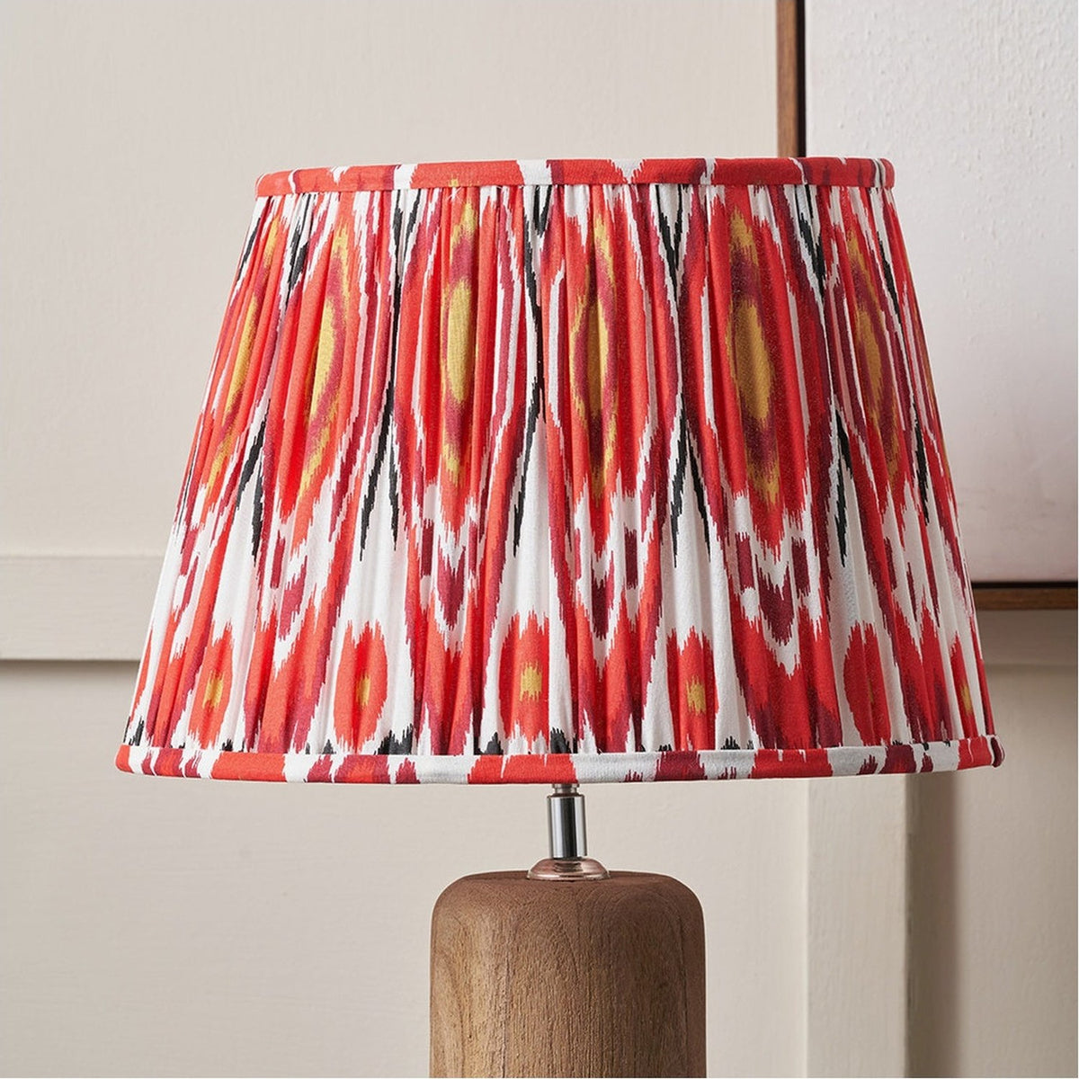 Izara Red Ikat Pleated Tapered Lampshade in 30cm, fabric with red, white and black ikat pattern, shown on a wooden table lamp base.