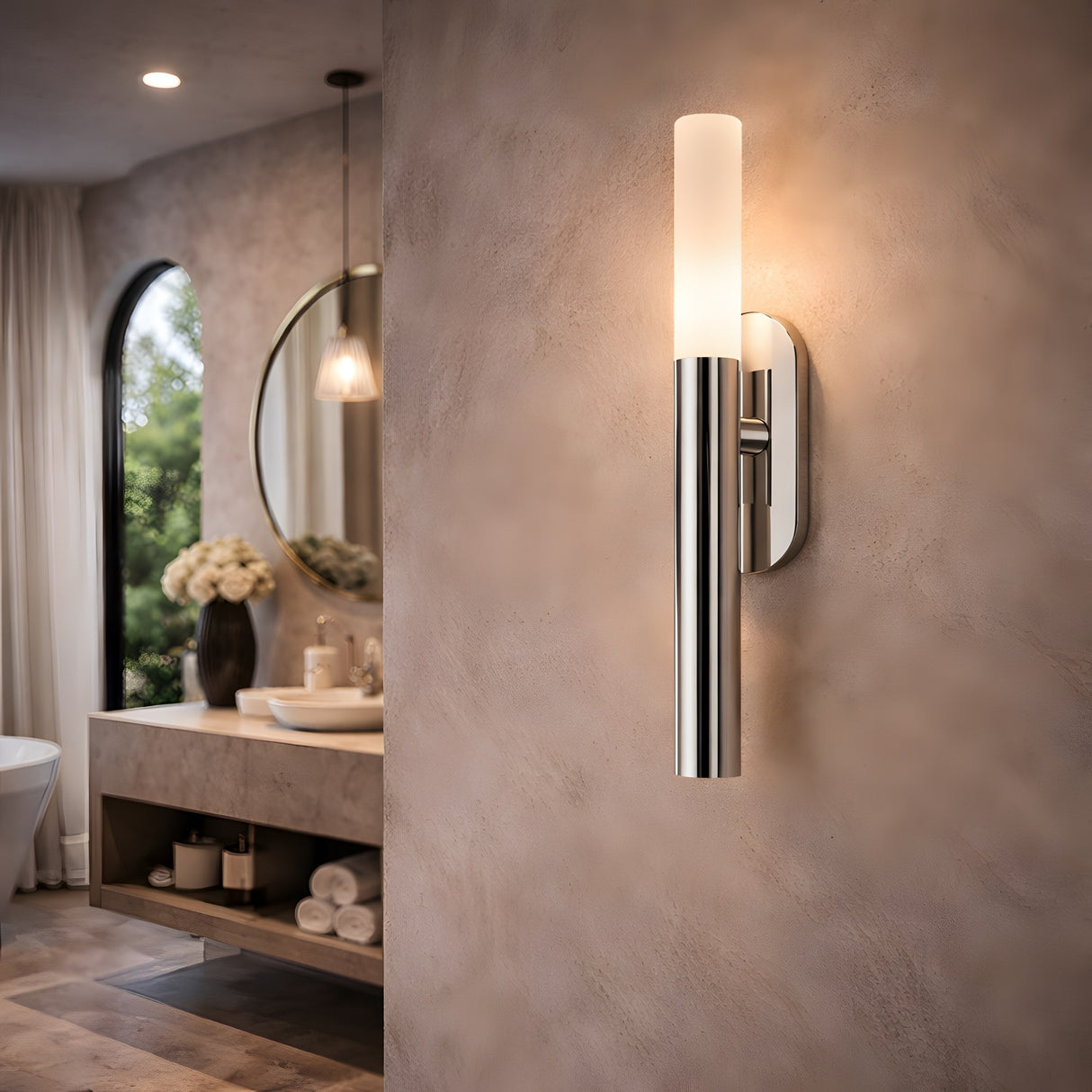 Modern bathroom featuring the Aurelian LED Vertical Column Alabaster Wall Light in satin nickel on a textured beige wall, with a vanity, round mirror, white flower vase, rolled towels, and a large window with sheer curtains.
