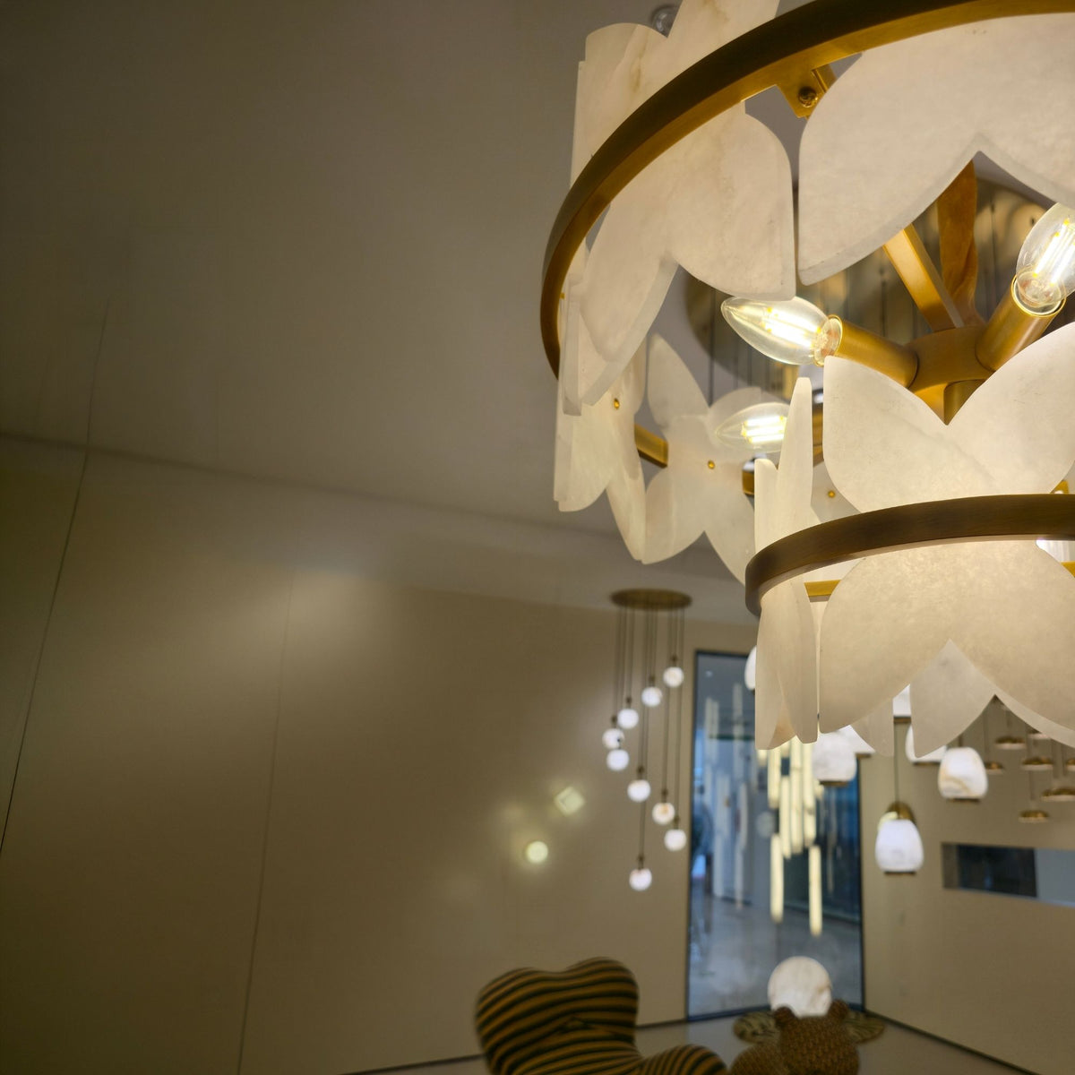 Petraia 2 Tier Floral Alabaster Chandelier in brushed brass, close-up of stone petal tiers and lit bulbs in a room setting.
