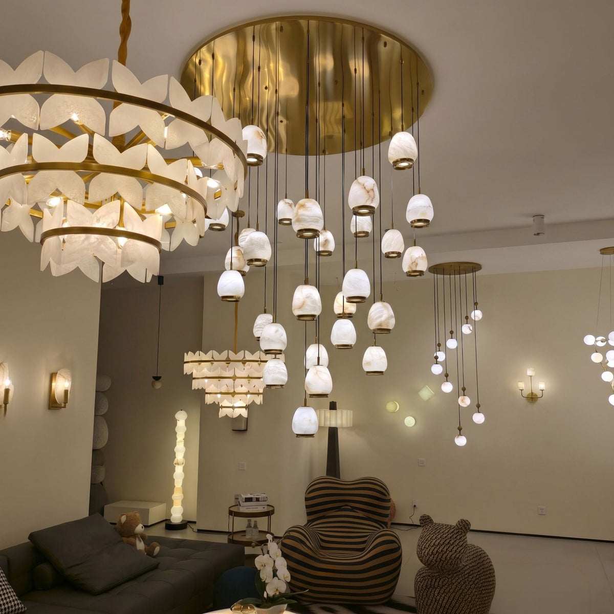 Aurevia 31-light LED alabaster chandelier with brushed brass canopy and cables, pebble-shaped drops shown suspended in a living room setting.