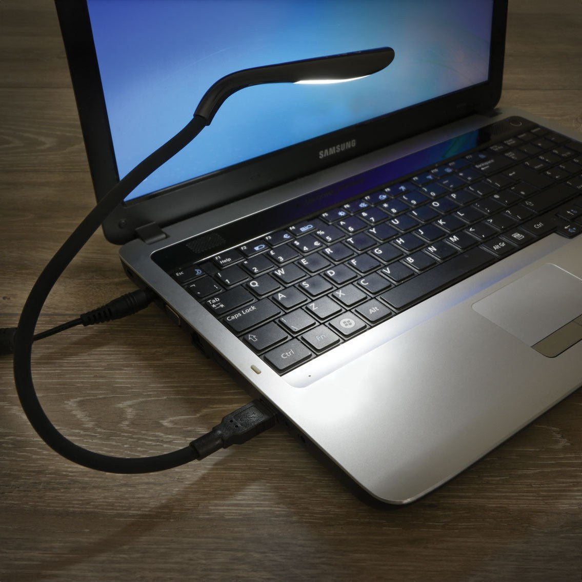 LYYT flexible USB LED lamp in black plugged into the side of a Samsung laptop, gooseneck stem bent over the screen to light the keyboard.