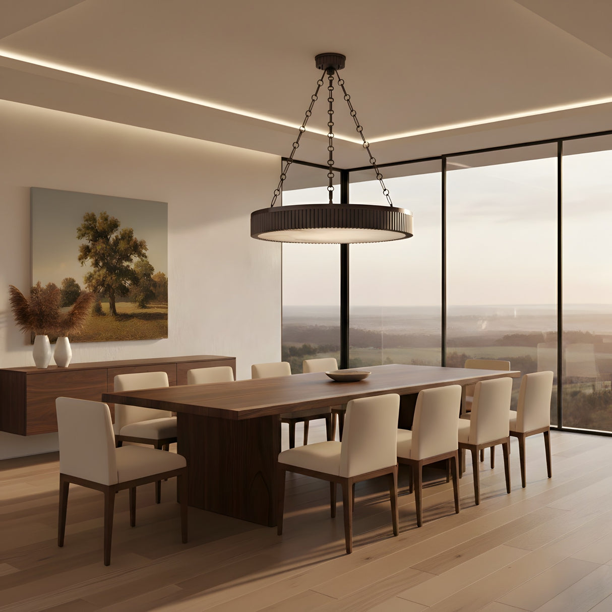 A modern dining room features a large wooden table, eight white cushioned chairs, the Heliora LED Chain-Suspended Disc Alabaster Chandelier – Matte Black, a sideboard with vases, a landscape painting, and floor-to-ceiling scenic windows.