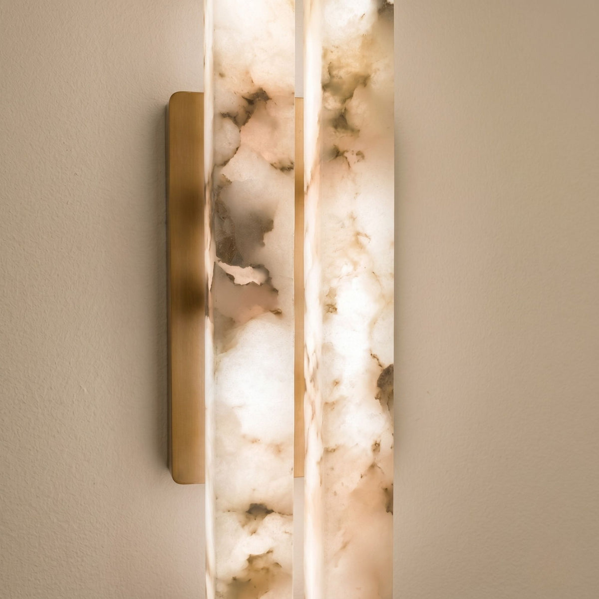 Close-up of the Selvara LED Medium Alabaster Double Wall Light, showing two vertical alabaster bars glowing warm white beside a brushed brass backplate on a neutral wall.