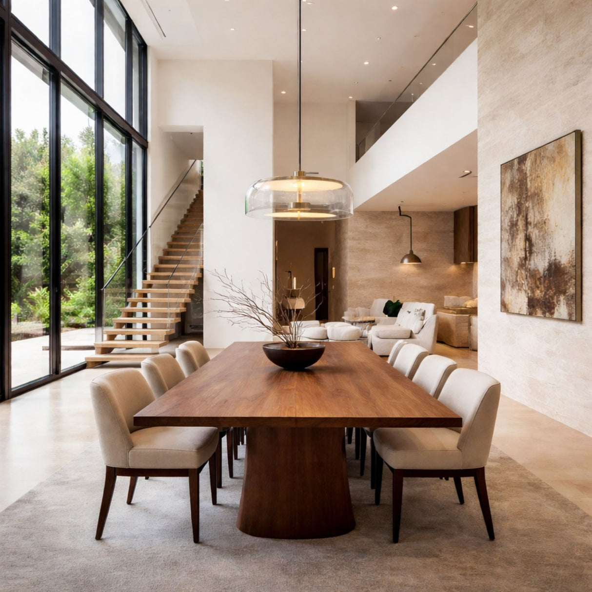 A modern dining room with a large wooden table, eight upholstered chairs, floor-to-ceiling windows, and the Blossom LED Glass Pendant Light - Gold as a centerpiece. A staircase and contemporary art enhance the open, airy atmosphere.