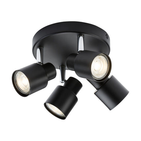 The Quad Spotlight - Matt Black is a ceiling light fixture with a modern matte black finish that features four adjustable directional cylindrical heads. Each spotlight emits bright white light and is mounted on a sleek, circular base, making it an ideal choice for contemporary interiors.