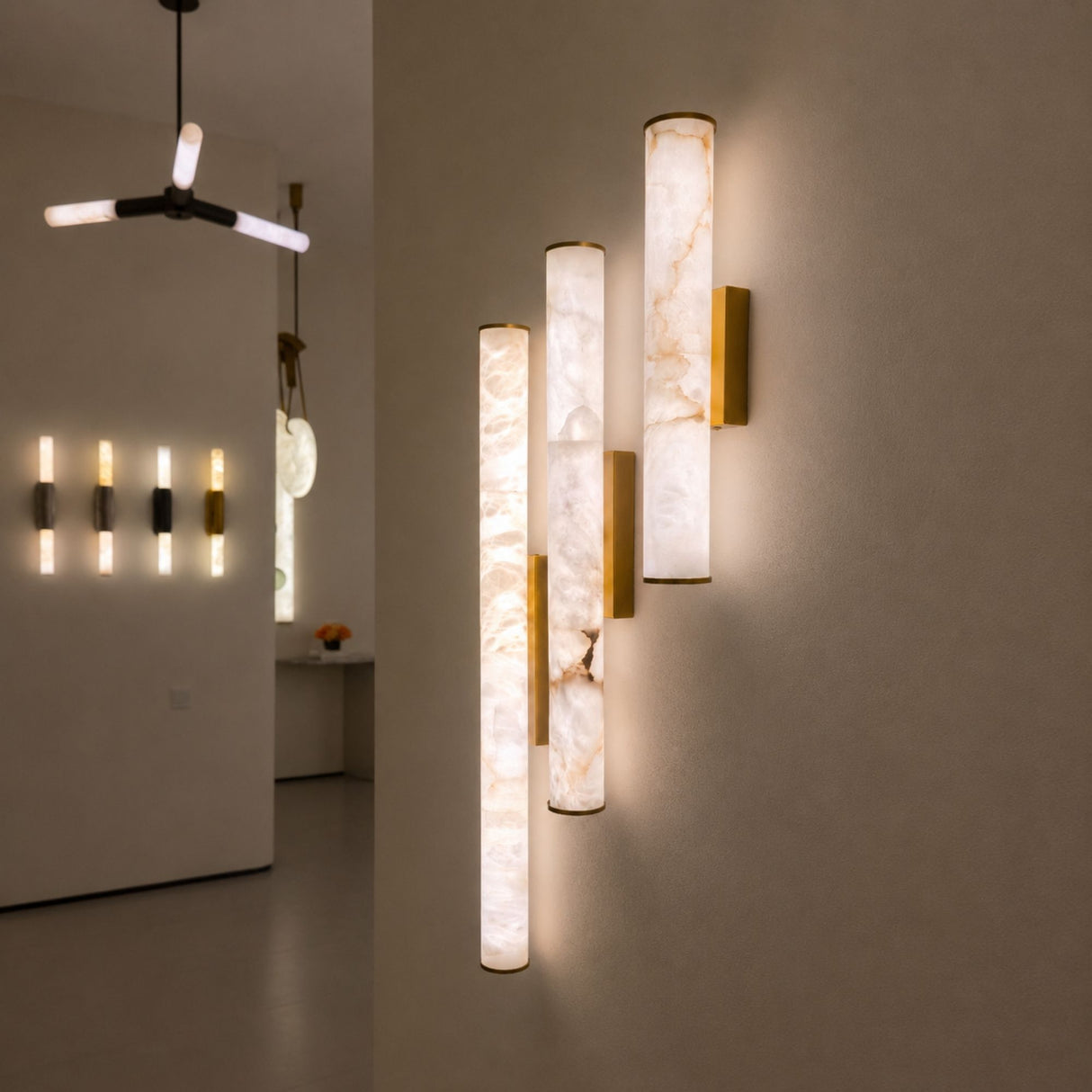 Montavo 800mm LED alabaster tube wall lights with brushed brass caps and backplates, shown illuminated in a staggered vertical arrangement on a hallway wall.