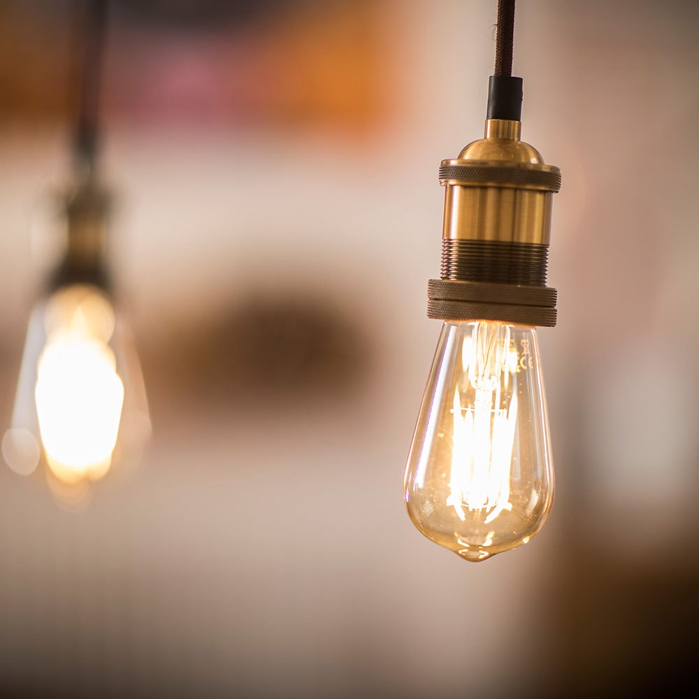LYYT ES pendant light in antique copper with knurled E27 lamp holder, braided cable and lit Edison filament bulb, second pendant glowing in the background.