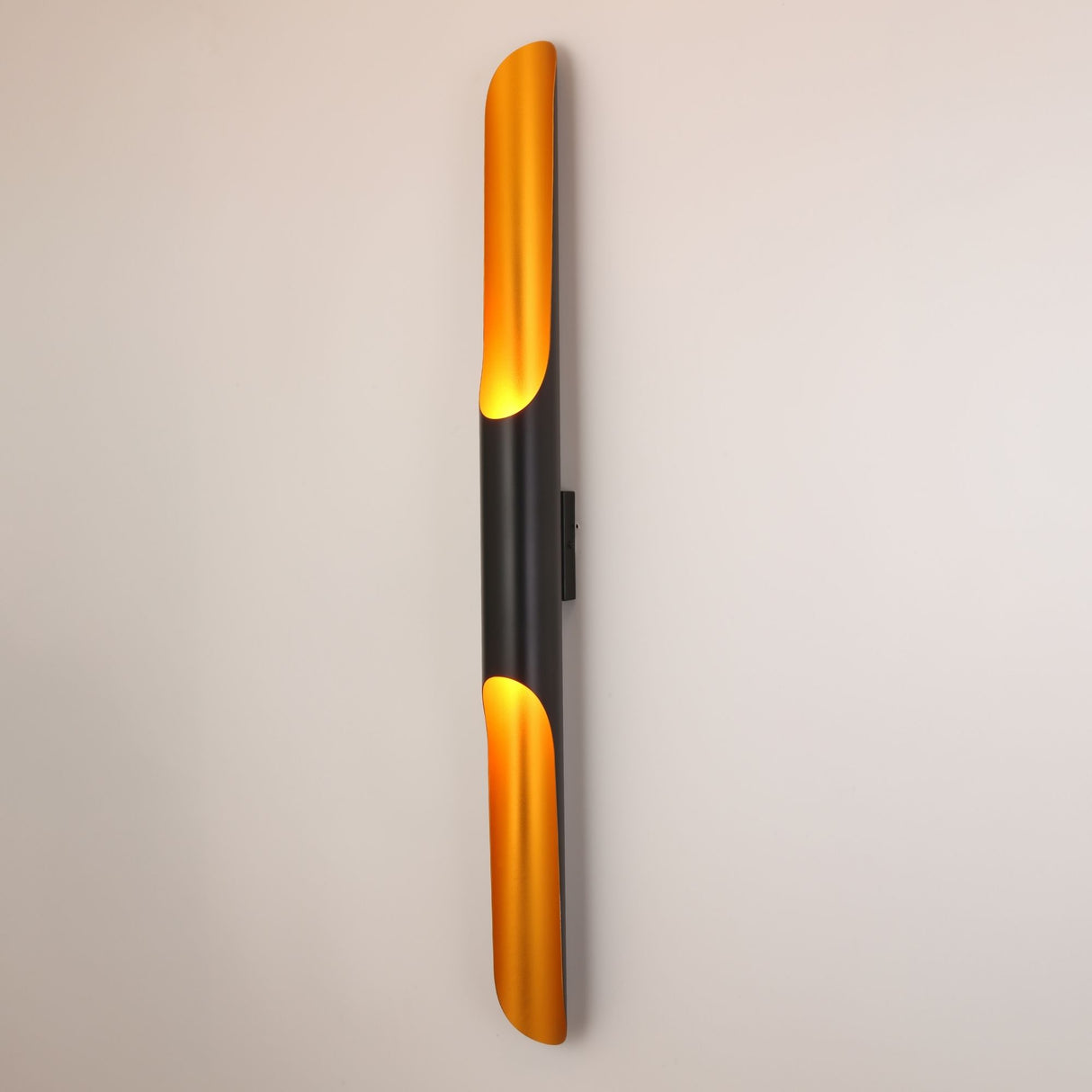Niori Stealth 2 Light Wall Light mounted vertically, featuring a slim matt black tubular body with brushed brass scoops at each end casting warm light.