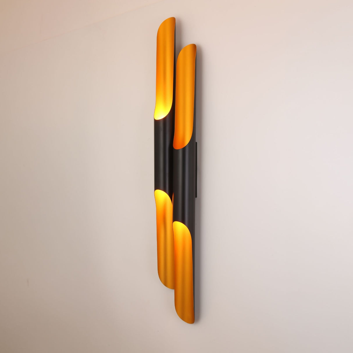 Niori Stealth 4 Light wall light with four angled tubular arms in matt black and brushed brass, mounted vertically on a pale wall and lit warmly.