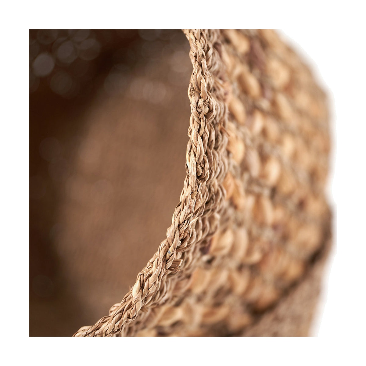 Close-up of a natural seagrass and water hyacinth tall basket showing its woven wicker texture and braided rim edge against a plain background.