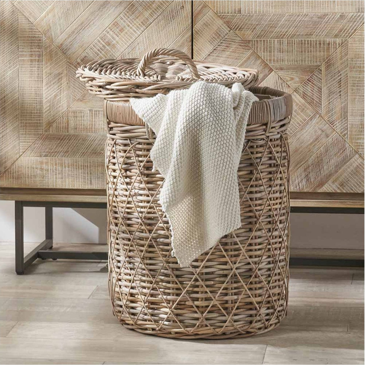 Round brown rattan linen basket, 42cm, with woven lid and handle, holding a folded white knit blanket in a room with a wood-panelled wall.
