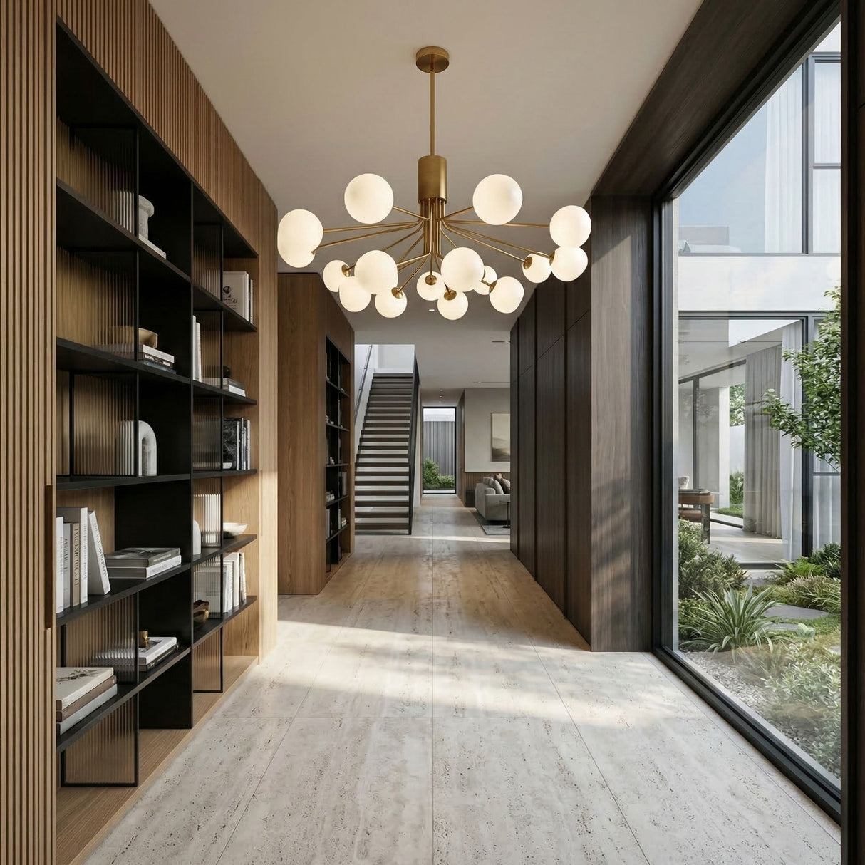 A modern hallway with tall bookshelves on the left, a floor-to-ceiling window on the right, beige tile flooring, and an elegant Ivy 18 Light Chandelier - Brass overhead, with a staircase leading to an upper floor in the background.