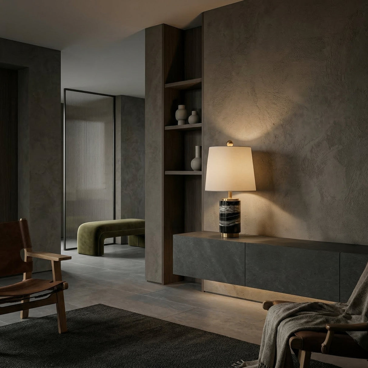 A modern, minimalist living room with dark textured walls, a floating console table, wooden chairs, built-in shelves with vases, and a green bench next door. Warm lighting and the Valmera 1 Light Cylinder Marble Table Lamp - Brass & Black create a cozy vibe.
