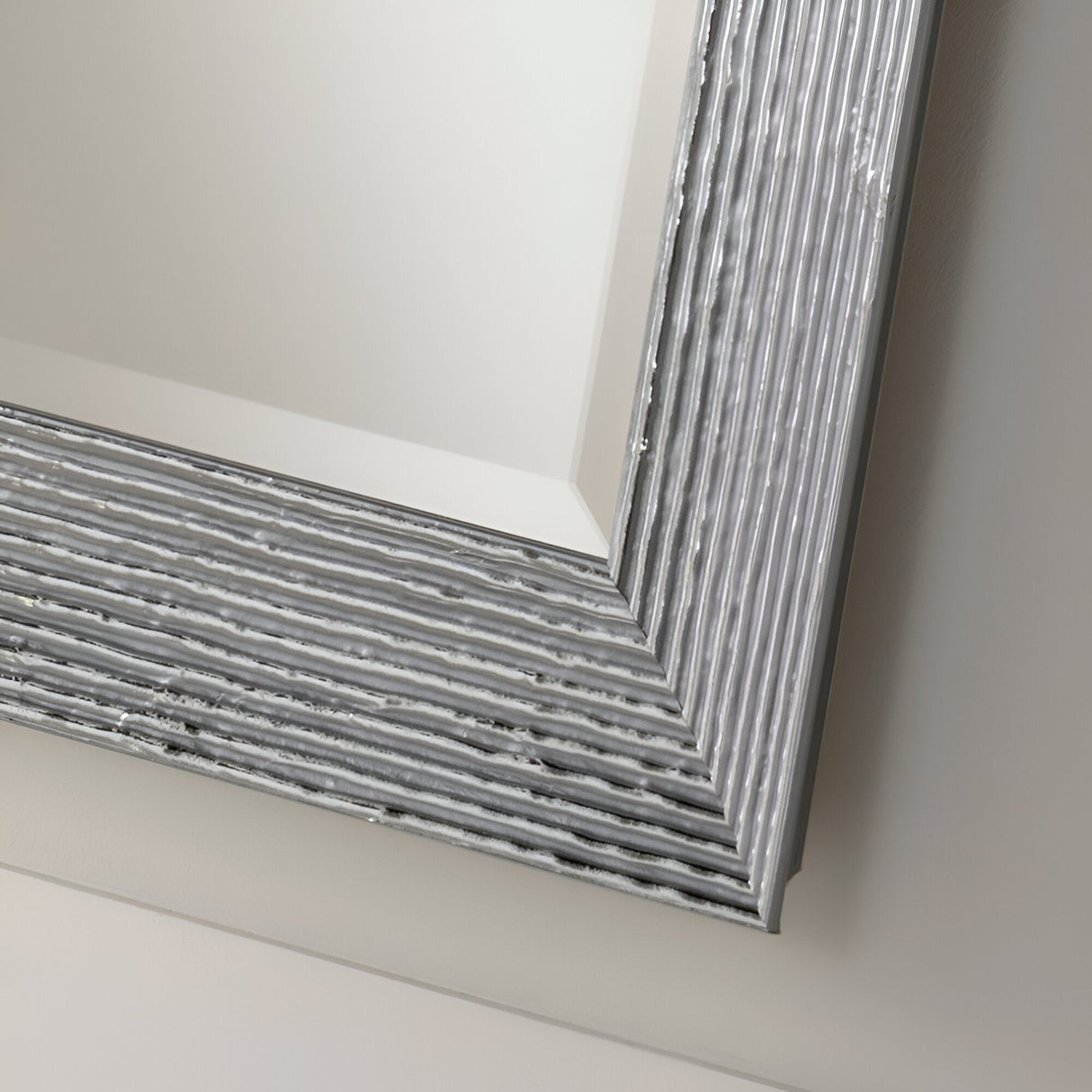 Close-up of the Charm Rectangle Wall Mirror - Silver, showcasing its textured, metallic frame. The minimalist frame displays ribbed horizontal lines that contribute to the contemporary elegance and sleek appearance of the mirror. It stands out against a light, neutral background.
