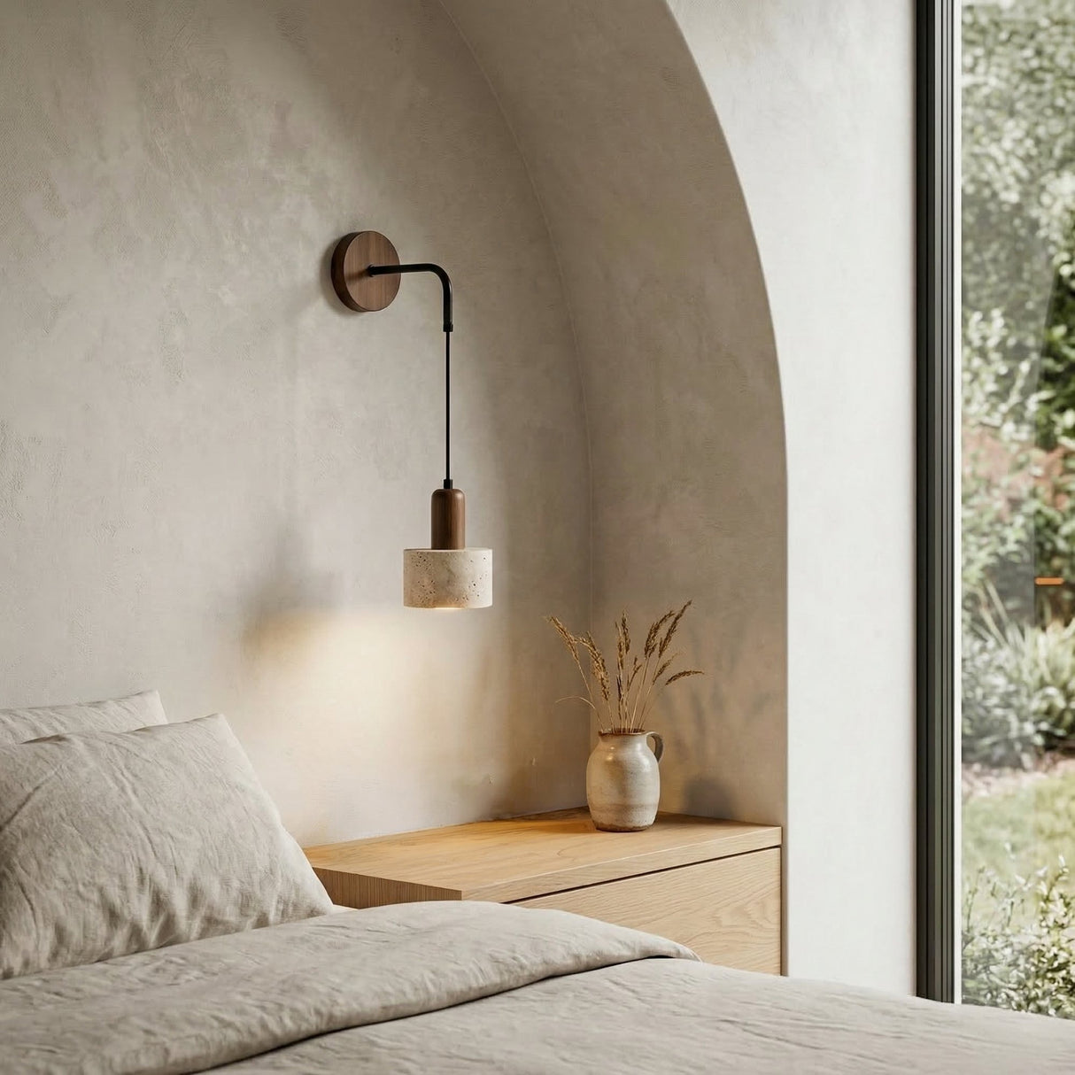 Minimalist bedroom with light beige bedding, a wooden nightstand holding a vase of dried grasses, the Torvella 1 Light Hanging Drum Travertine Wall Light in walnut brown & light beige, an arched alcove, and large window revealing greenery.