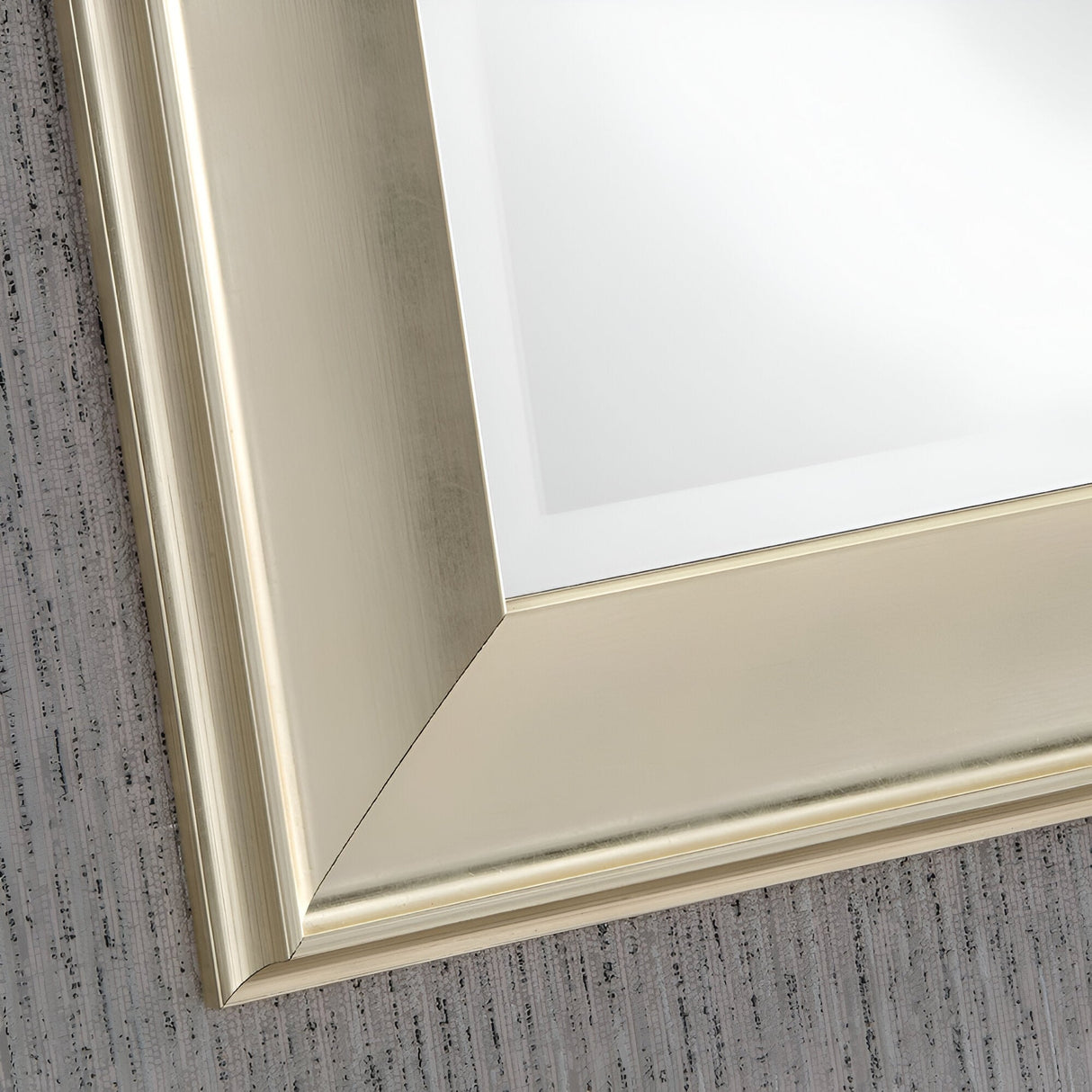 Close-up of a luxury decor brushed gold metallic picture frame corner against a textured gray background. The Pulse Rectangle Wall Mirror - Champagne frame features a smooth, reflective surface with a polished finish, emphasizing its clean lines and elegant design.