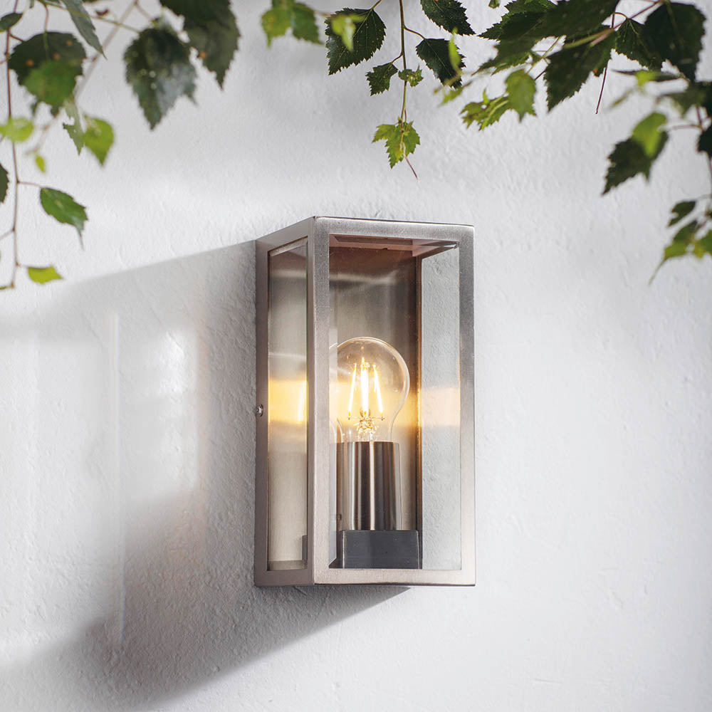 Endon Castwick silver box lantern wall light with bevelled glass panels and E27 filament bulb, mounted on a white wall beneath green foliage.