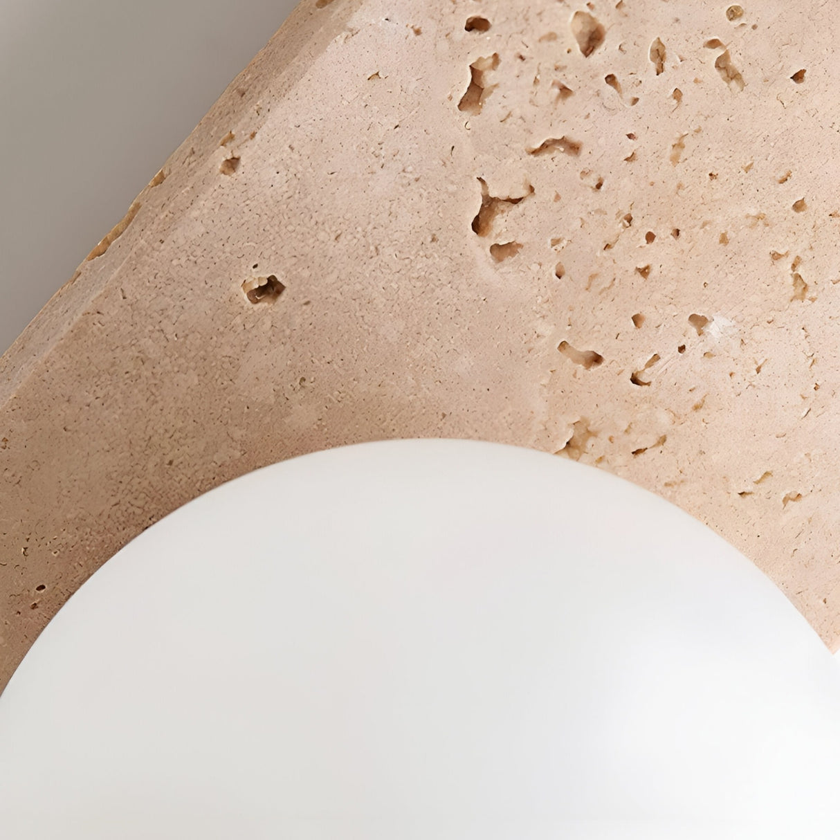 Close-up of the Virella 3 Light Vertical Travertine Wall Light in light beige, showing its textured surface with small holes, mounted diagonally above a smooth white object in the lower foreground.