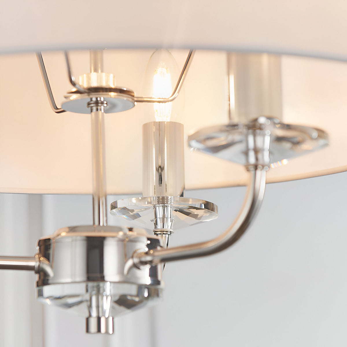 Close-up of Endon Castdon 3 light pendant showing polished nickel arms, K9 crystal bobeches, an E14 candle lamp, and white faux silk shade.