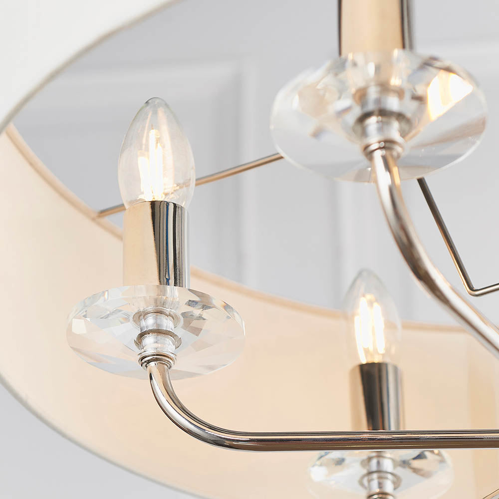 Close-up of the Castdon 6 Light Pendant in nickel, showing candle bulbs, crystal bobeche discs, and white faux silk shades against a light background.