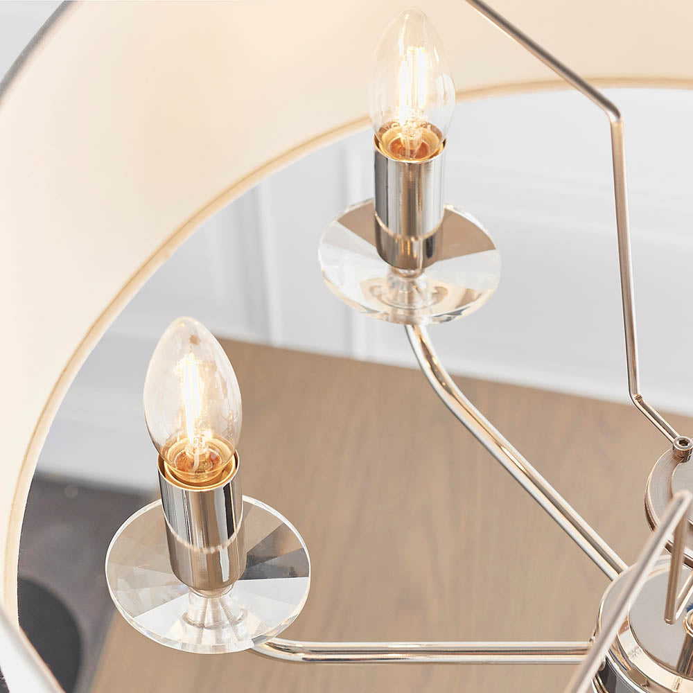 Close-up of the Castdon 6 light pendant, nickel arms with crystal bobeches holding E14 candle bulbs beneath white faux silk shades.
