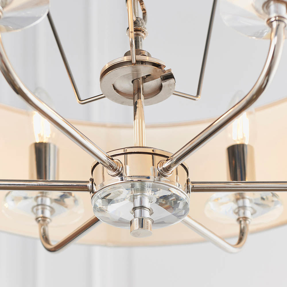 Close-up of the Castdon 6 Light Pendant's nickel frame and central hub, showing crystal bobeche detail and E14 candle bulbs beneath white shades.