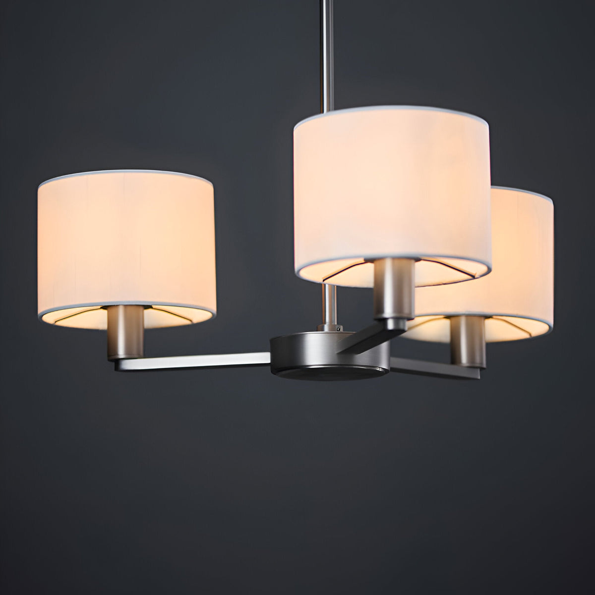 Bexley 3 Light Pendant in matt nickel, three curved arms holding cylindrical white fabric shades, shown against a dark background.