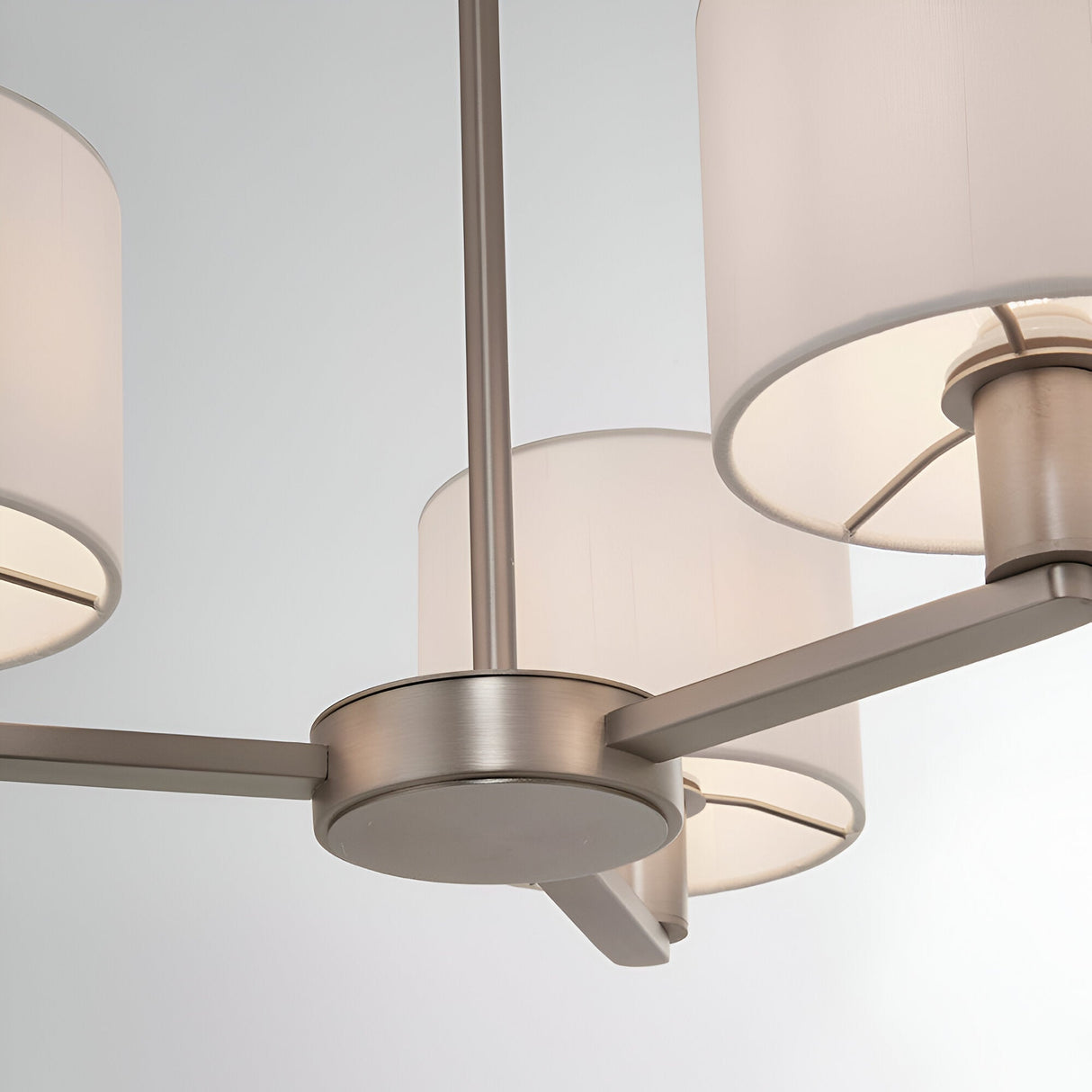 Close-up of the Bexley 3 Light Pendant in matt nickel, showing curved metal arms with white faux silk cylinder shades against a plain light background.