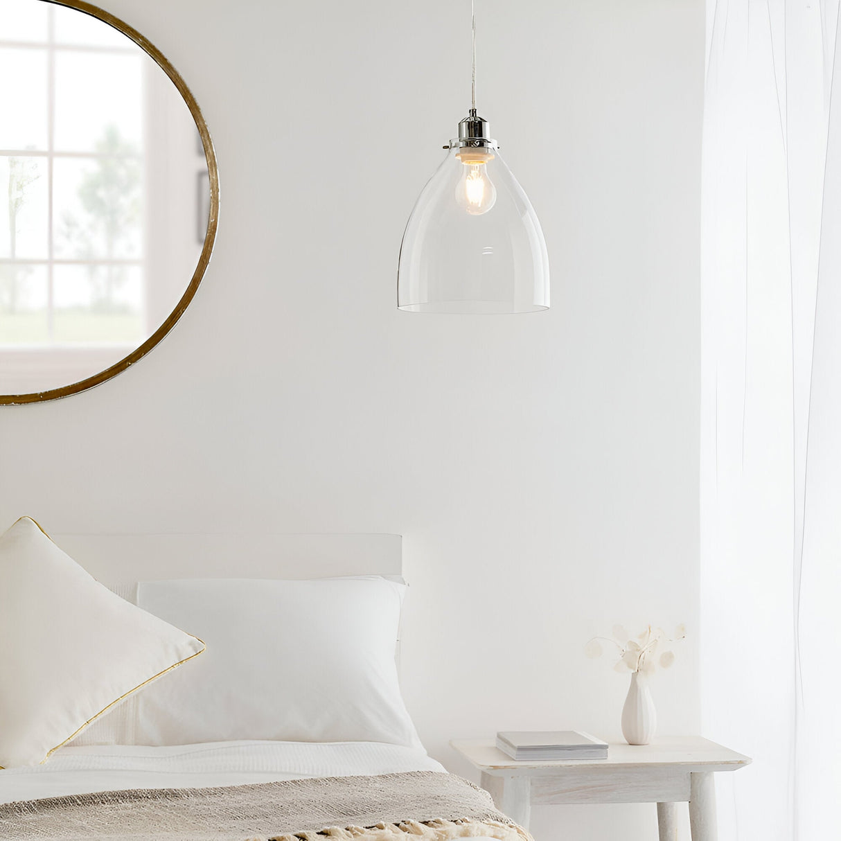 Endon Brackmere clear glass pendant light with polished chrome gimbal and exposed filament bulb, hanging beside a round mirror above a white bed.