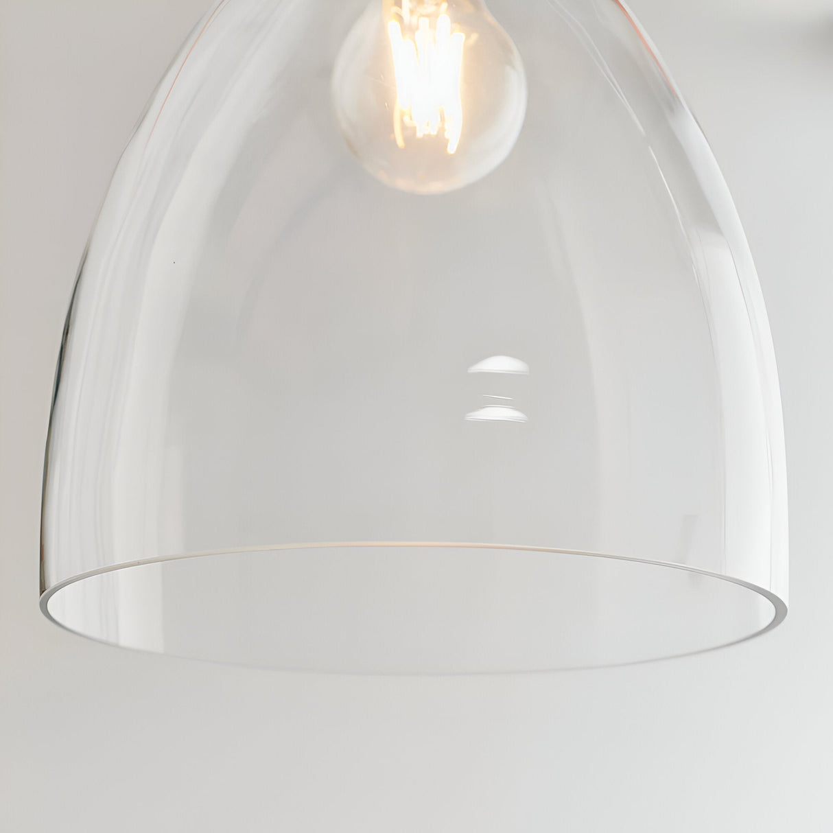 Close-up of the Endon Brackmere clear glass bell-shaped pendant shade with polished chrome trim and lit E27 filament bulb against a light background.