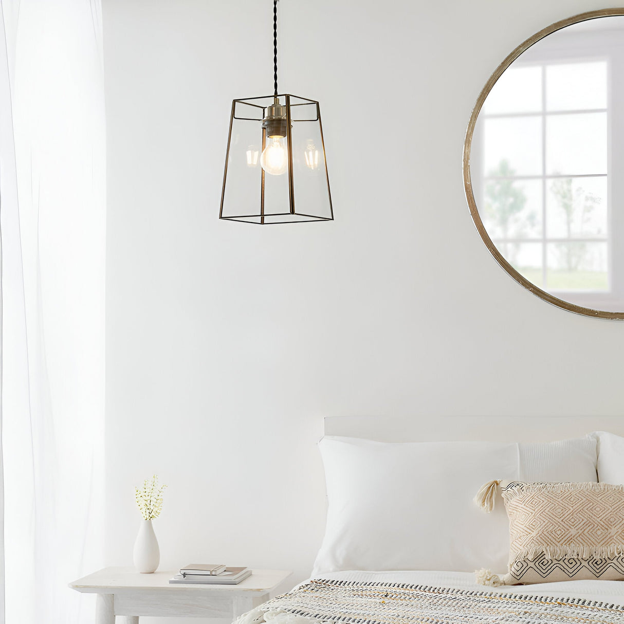 Endon Aldwell antique brass pendant light with faceted clear glass shade, hung in a bright white bedroom beside a round wood-framed mirror.