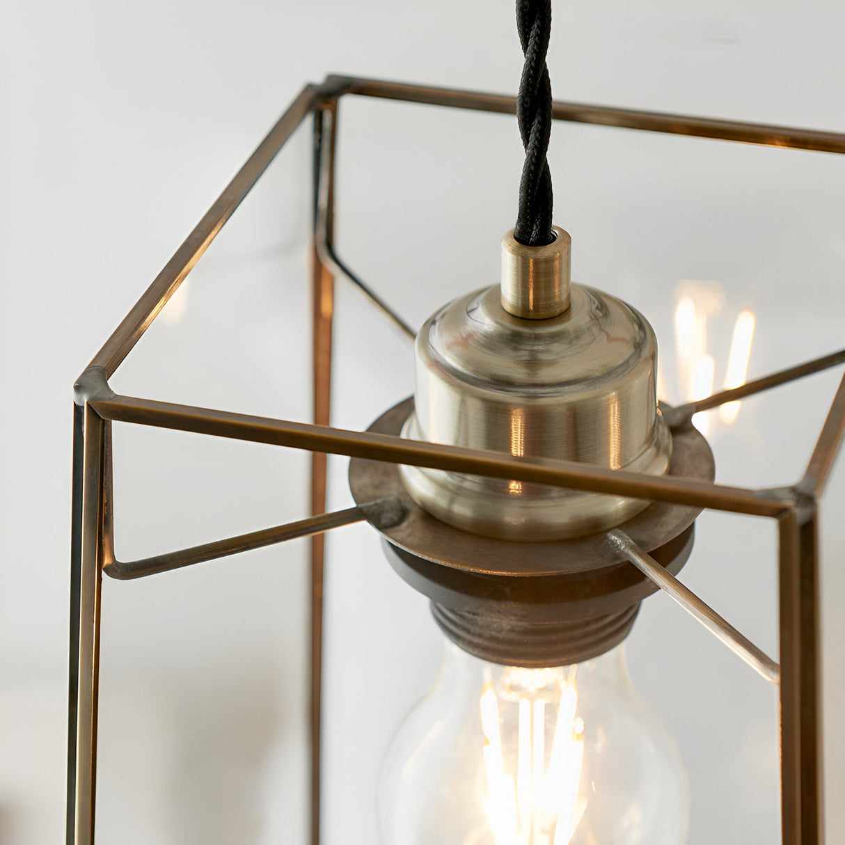 Close-up of Endon Aldwell pendant light showing antique brass lamp holder, angular glass frame, and glowing filament E27 bulb.