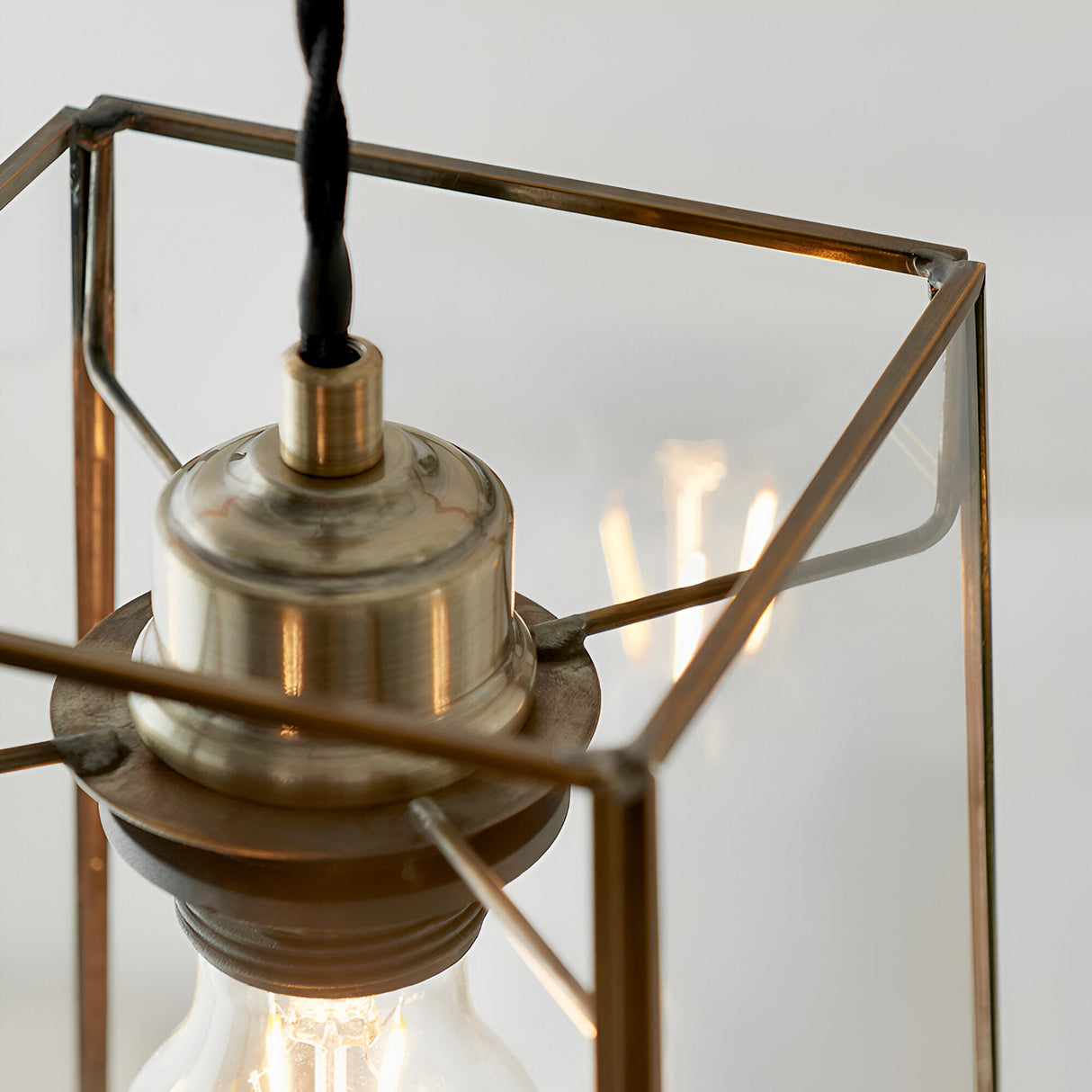 Close-up of the Endon Aldwell pendant light showing the antique brass lampholder, faceted clear glass frame and filament bulb inside.