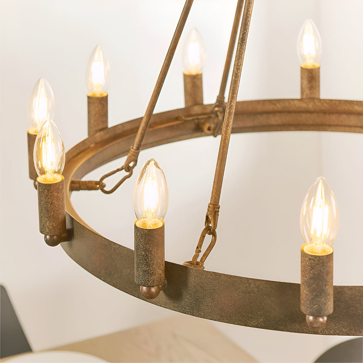 Bevgrove 12-light pendant close-up showing an aged metal ring frame with candle-style E14 fittings and rustic support chains against a plain background.