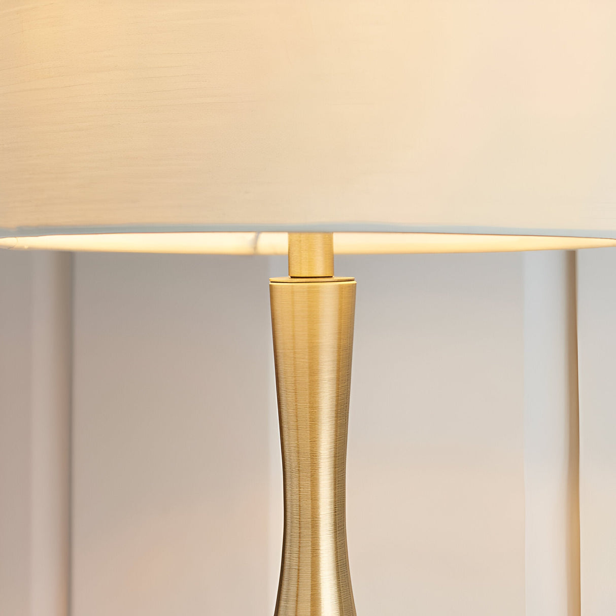 Close-up of the Endon Chartbury LED table lamp showing its slim brushed brass stem and beige fabric drum shade illuminated with warm white light.