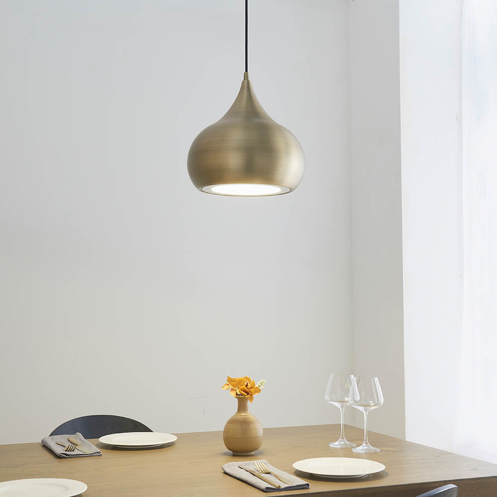 Endon Ashleigh pendant light with a curved matt brass shade and white diffuser, hung above a wooden dining table set with glasses and a flower vase.