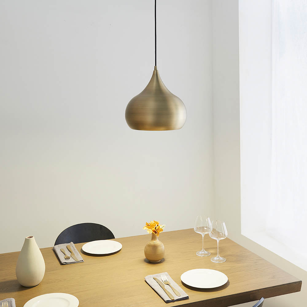 Endon Ashleigh brass pendant light with a curved teardrop shade hanging above a wooden dining table set with plates, wine glasses and a vase.