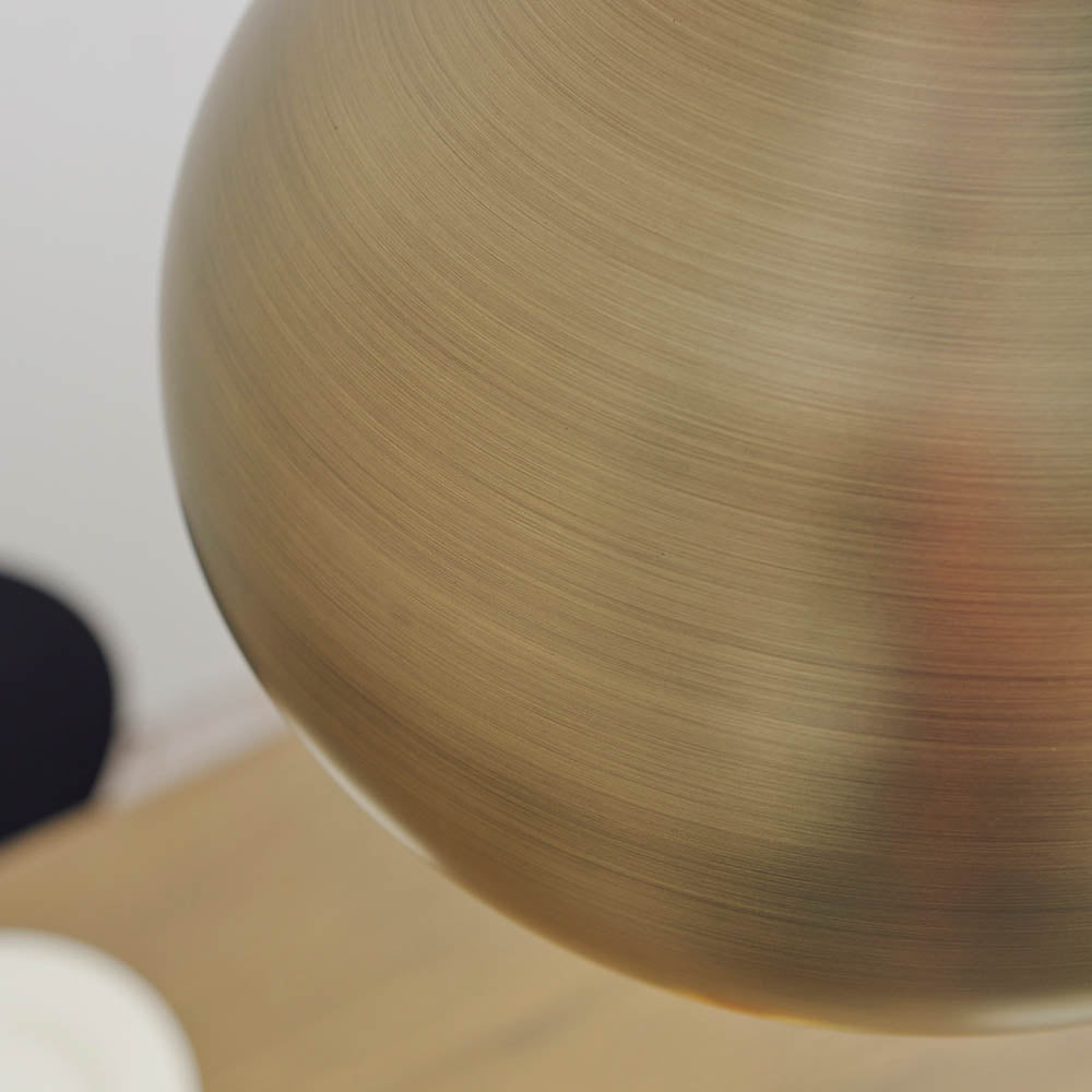 Close-up of the Endon Ashleigh pendant's spherical brass diffuser, showing the brushed matt antique brass finish against a pale wall.