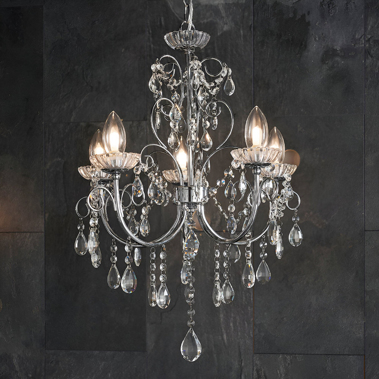 Endon Crandon 5 light bathroom chandelier in polished chrome with clear crystal droplets and beaded strands, shown against a dark slate tiled wall.
