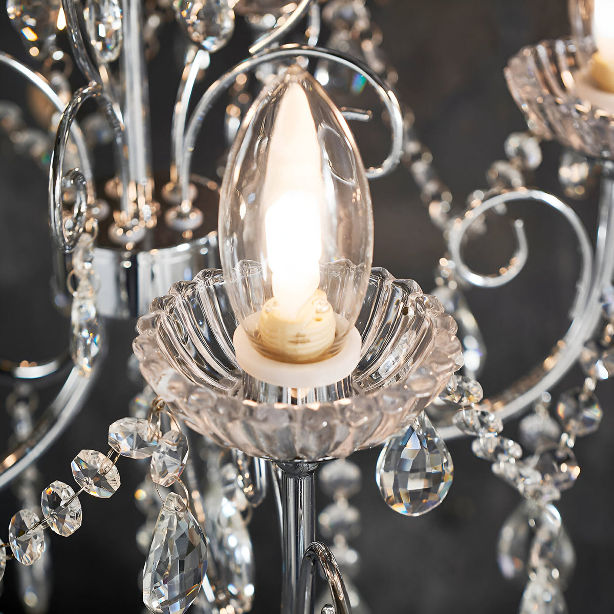 Close-up of Endon Crandon 5 Light Bathroom Chandelier in polished chrome, showing a lit G9 candle bulb seated in a fluted crystal cup with hanging droplets.