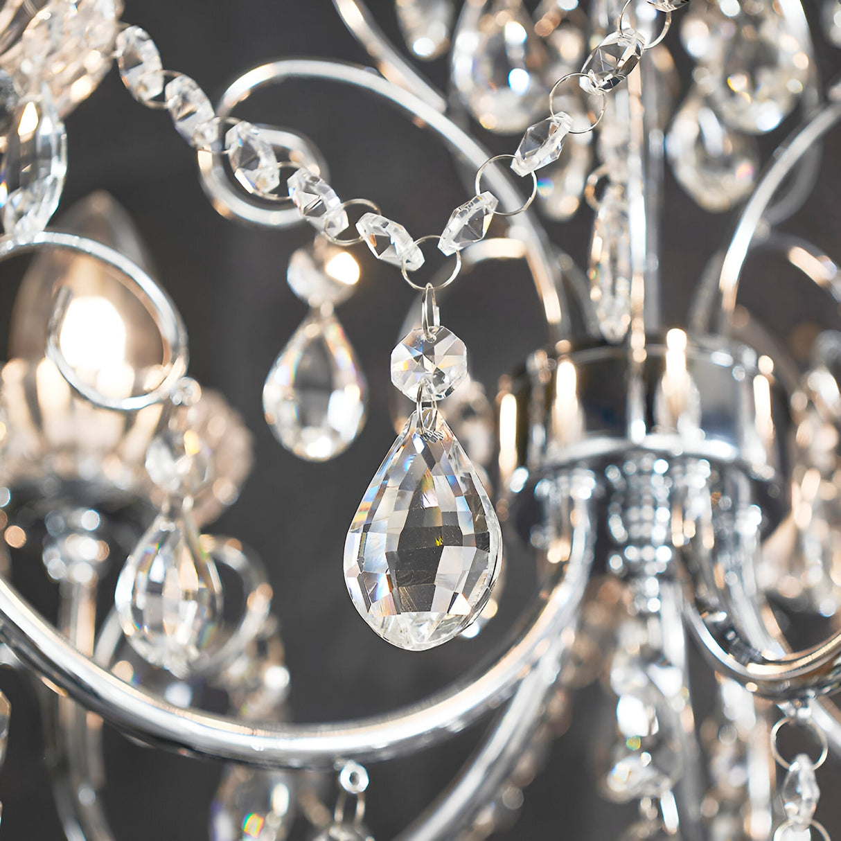 Close-up of the Endon Crandon bathroom chandelier showing polished chrome scrollwork, faceted crystal chain strands, and a clear teardrop crystal droplet.