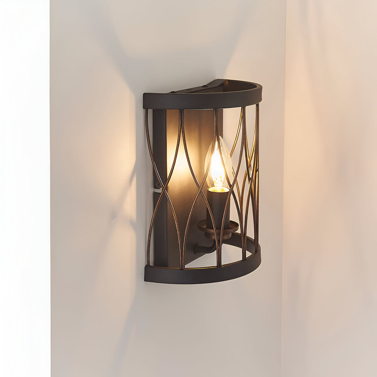Endon Hulton wall light in matt black and rustic bronze with a curved steel cage frame and single E14 candle bulb, mounted on a pale wall.
